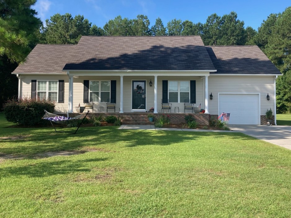 Front view of a single-story house with a porch, grassy yard, and a hammock.
